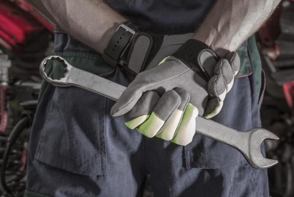 Mechanic standing in front of heavy trucking equipment holding a wrench with both hands behind his back