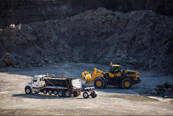 A gravel truck and a large yellow loader are operating in a rocky quarry.